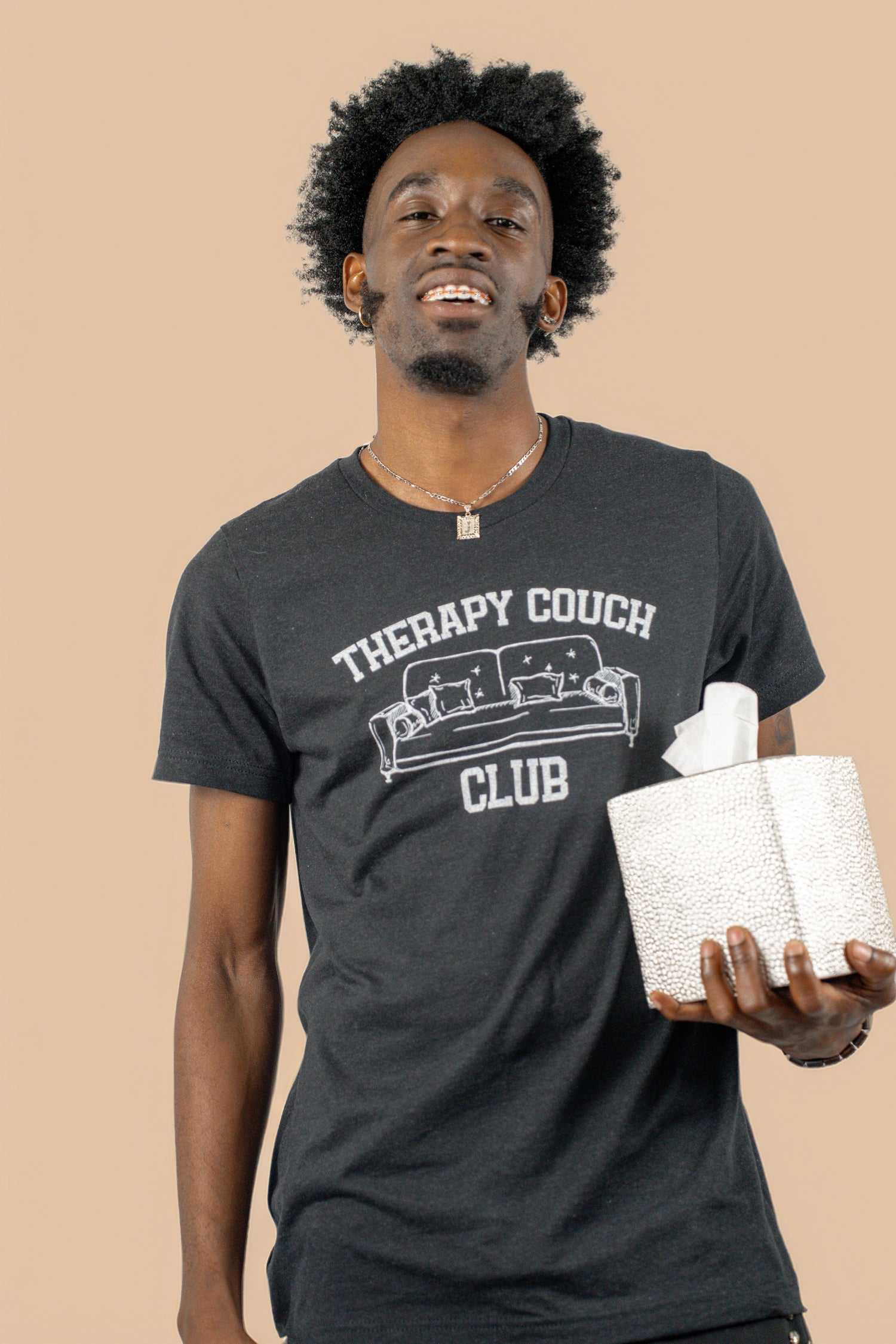 Model wearing a black “Therapy Couch Club” t-shirt while holding a textured tissue box, standing against a neutral beige background.