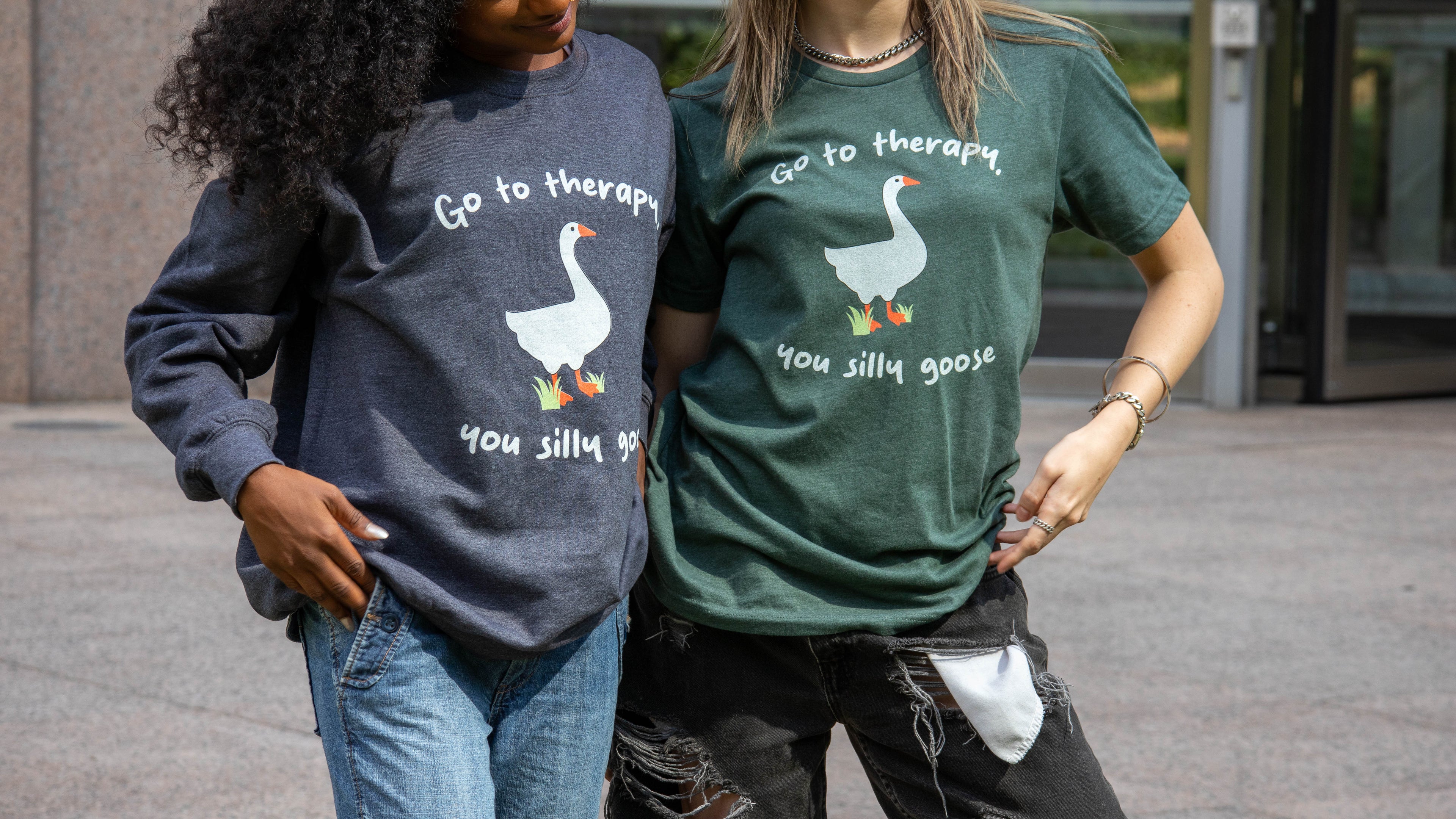 Two women wearing Layered Feels mental health affirmation t-shirts with a goose graphic and the phrase “Go to therapy, you silly goose,” promoting emotional wellness and therapy-inspired apparel.